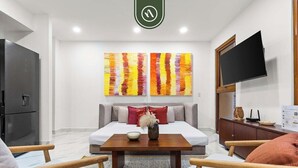 A modern living room with a sofa, a coffee table, a flat-screen TV, and two abstract paintings. - New 1 BR Condo - Rooftop Pool - Romantic Zone (Puerto Vallarta)