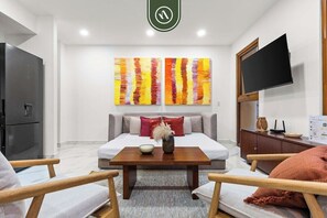 A modern living room with a sofa, a coffee table, a flat-screen TV, and two abstract paintings. - New 1 BR Condo - Rooftop Pool - Romantic Zone (Puerto Vallarta)