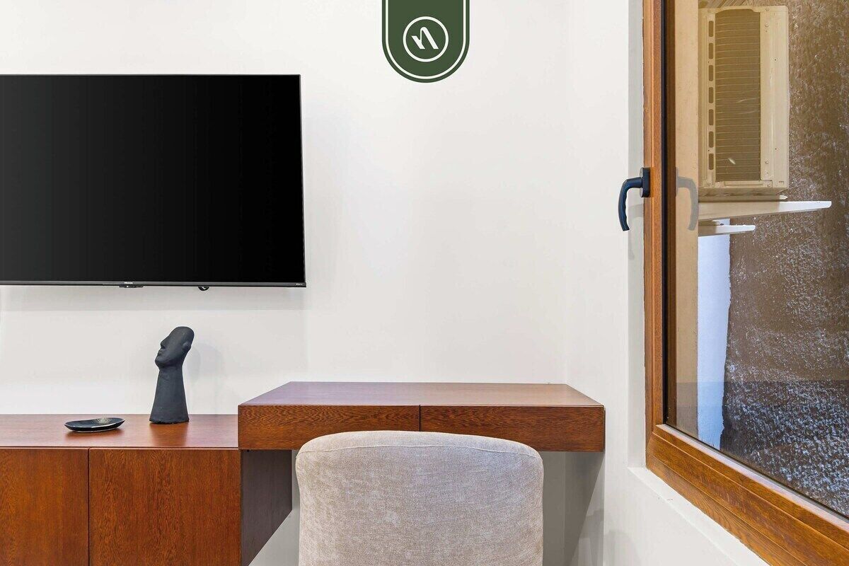 Une chambre dotée d’un téléviseur à écran plat fixé au mur, d’un bureau en bois avec une chaise et d’une fenêtre à vitrage dépoli.