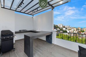 Un balcón con vista a la ciudad, una parrilla y una mesa de hormigón.