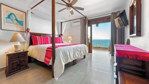 Ein Bett mit Baldachin, ein Balkon, ein Nachttisch aus Holz, ein Tisch mit roter Tischdecke und ein Gemälde an der Wand.