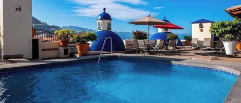 A pool area with a clear view of the sea, lounge chairs, and potted plants.