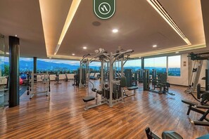 Ein Fitnessstudio mit verschiedenen Trainingsgeräten, Holzboden und großen Fenstern mit Blick auf die Stadt.