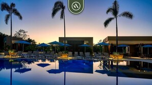 A pool with lounge chairs and umbrellas, palm trees, and a modern building.