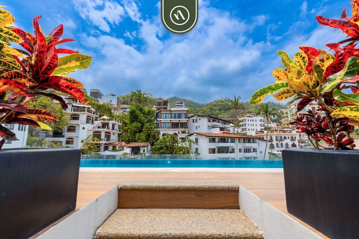 A poolside view with a clear sky, a pool, and buildings in the background.
