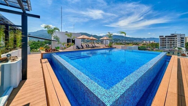 Une piscine rectangulaire bordée de carreaux, entourée d’une terrasse en bois, et offrant une vue sur les montagnes en arrière-plan.