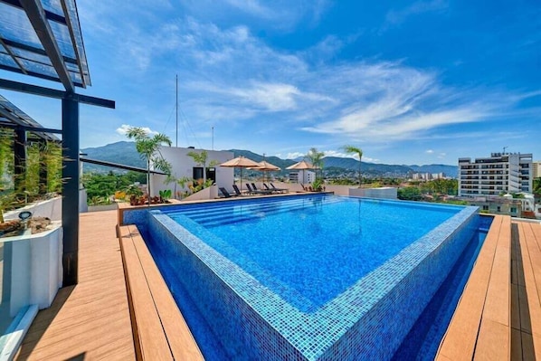 A rectangular swimming pool with a tiled edge, surrounded by wooden decking, and a view of mountains in the background.