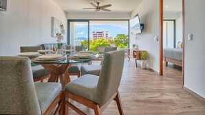 Un espace repas moderne avec une table en verre, des chaises à revêtement gris et un ventilateur de plafond.