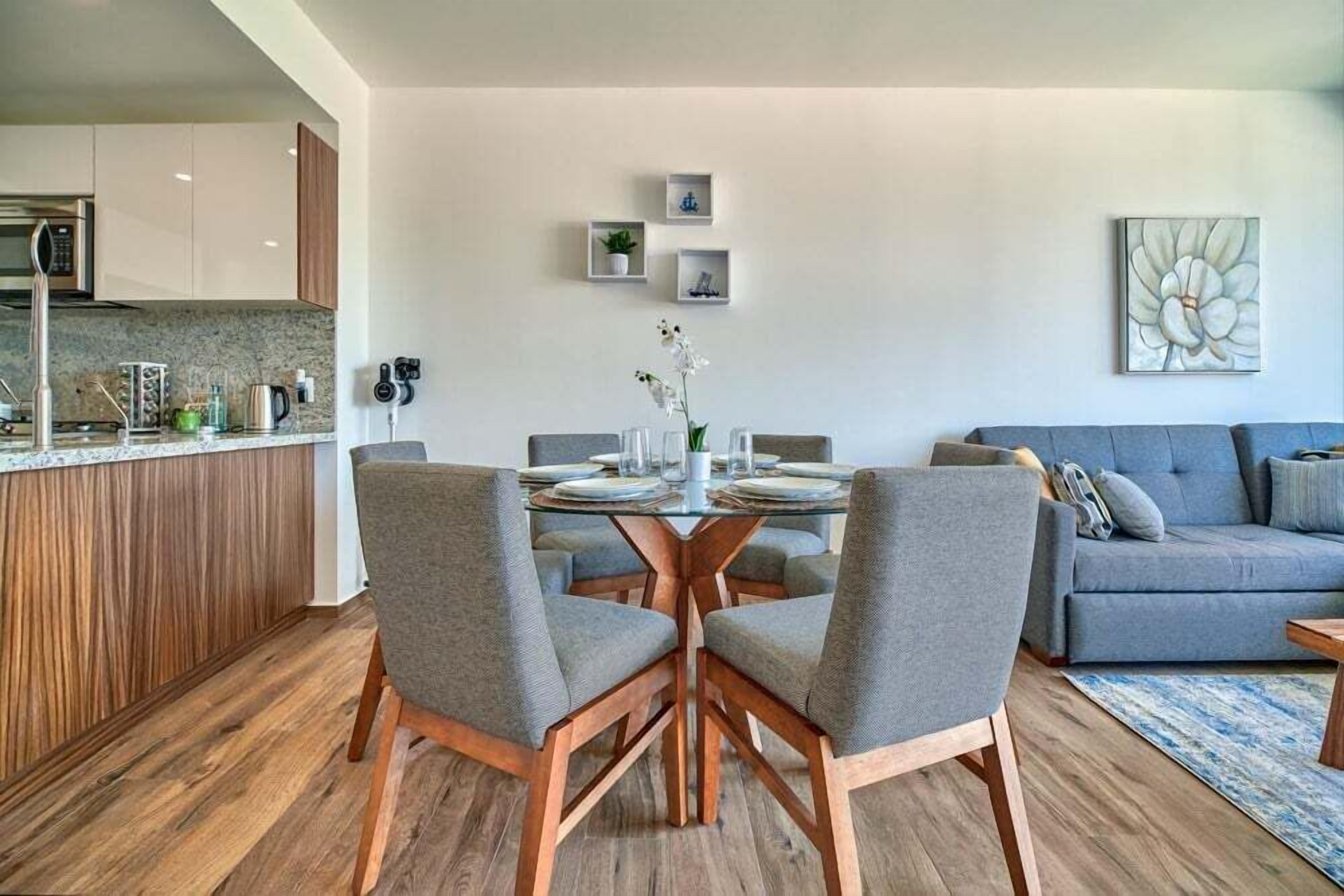 A modern kitchen with a dining area, a grey sofa, and a wall-mounted artwork.