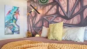 A modern bedroom with a large bed, a colorful abstract painting, and a unique wall design. - Two Story 2 BR Penthouse - Pool - Ocean View (Puerto Vallarta)