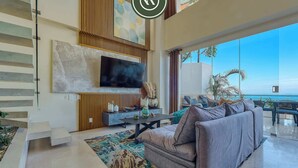 A modern living room with a large TV, a sofa, and a view of the ocean. - Two Story 2 BR Penthouse - Pool - Ocean View (Puerto Vallarta)