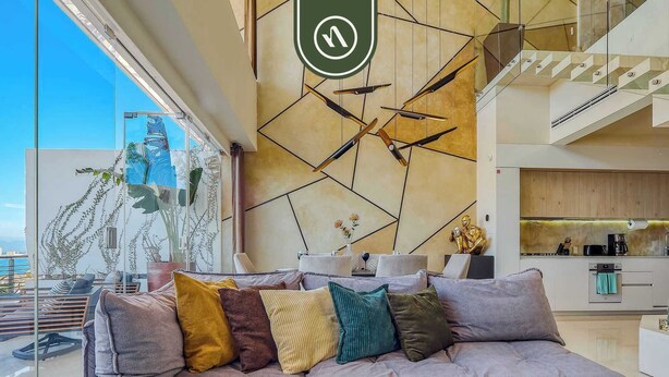 A modern living room with a sofa, a teal throw blanket, and a dining area with a kitchen in the background. - Two Story 2 BR Penthouse - Pool - Ocean View (Puerto Vallarta)