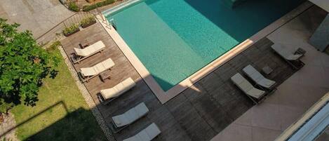 A rectangular swimming pool with lounge chairs and a wooden deck.
