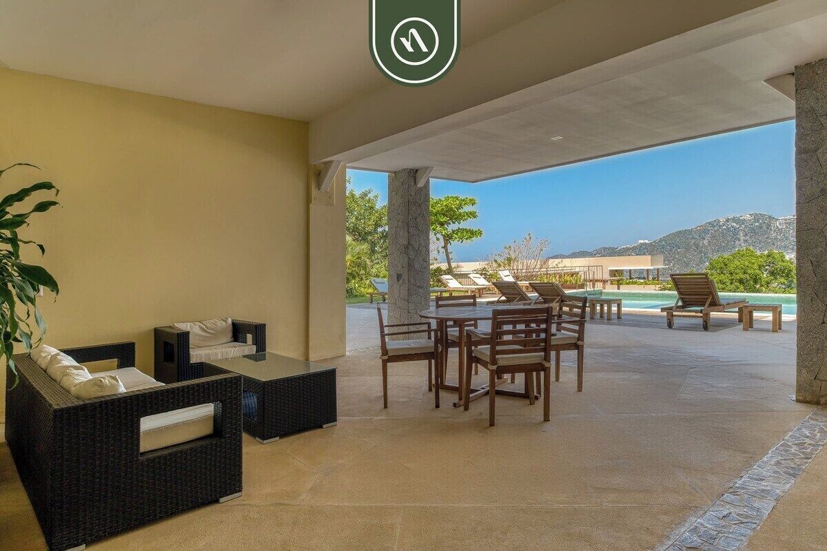A sunlit outdoor seating area with wicker furniture and a view of a pool and mountains.