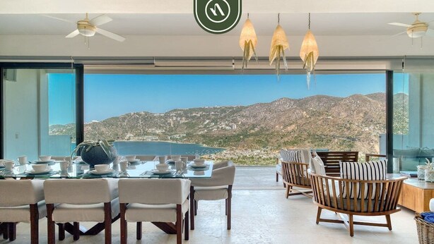 A dining area with a table set for four, chairs, and hanging pendant lights. - Luxury 4 BR Condo - Amazing Bay View - Pool (Acapulco)