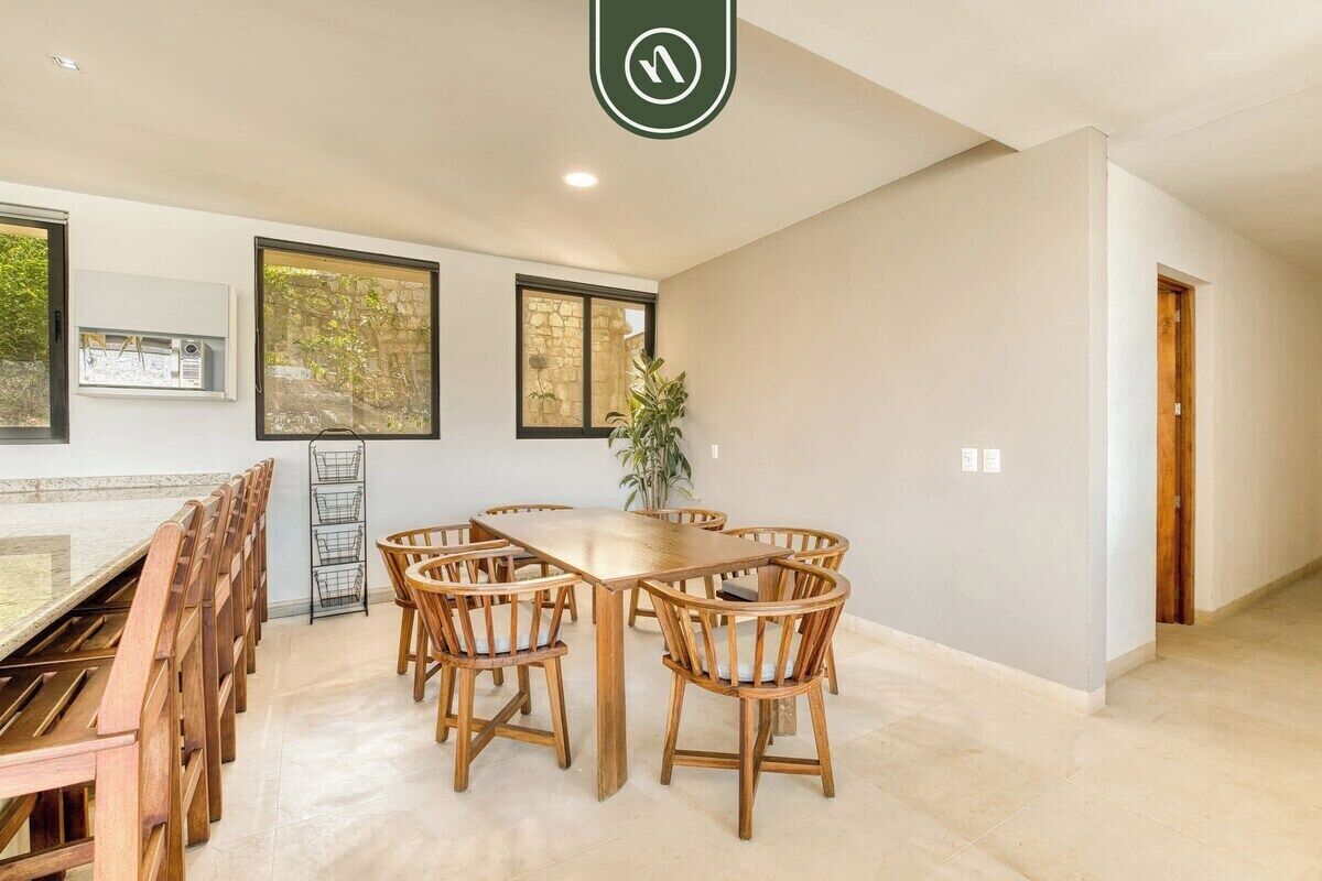 Un amplio comedor con una larga mesa de madera y sillas, ventanas grandes y una planta.