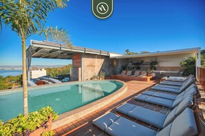 A modern pool area with lounge chairs, a covered seating area, and a view of the sea. - 3 BR Condo - Private Terrace and Pool - Oceanview (Puerto Vallarta)