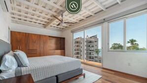 A bedroom with a bed, wooden wardrobe, ceiling fan, large windows, and a view of buildings. - 3 BR Condo - Private Terrace and Pool - Oceanview (Puerto Vallarta)