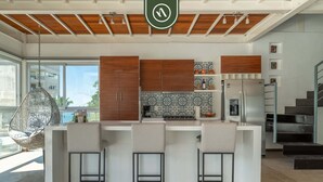 A modern kitchen with a central island, bar stools, wooden cabinets, and a patterned backsplash. - 3 BR Condo - Private Terrace and Pool - Oceanview (Puerto Vallarta)