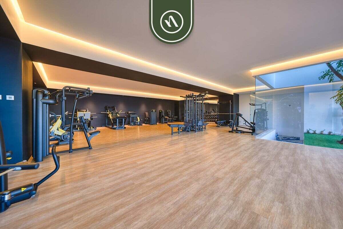 Ein modernes Fitnessstudio mit verschiedenen Trainingsgeräten, Holzboden und einem großen Fenster mit Blick ins Freie.