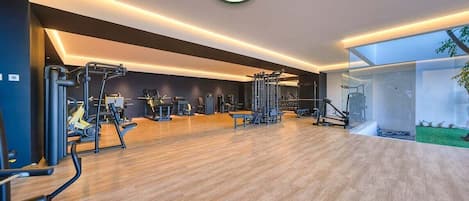 Ein modernes Fitnessstudio mit verschiedenen Trainingsgeräten, Holzboden und einem großen Fenster mit Blick ins Freie.