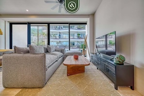A modern living room with a sofa, coffee table, TV, and a balcony view. - Luxury Studio in Romantic Zone - Infinity Pool (Puerto Vallarta)
