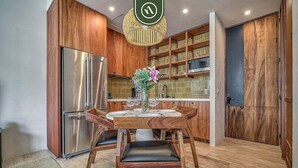 A modern kitchen with wooden cabinetry, a stainless steel refrigerator, a dining table with chairs, and a hanging light fixture. - Luxury Studio in Romantic Zone - Infinity Pool (Puerto Vallarta)