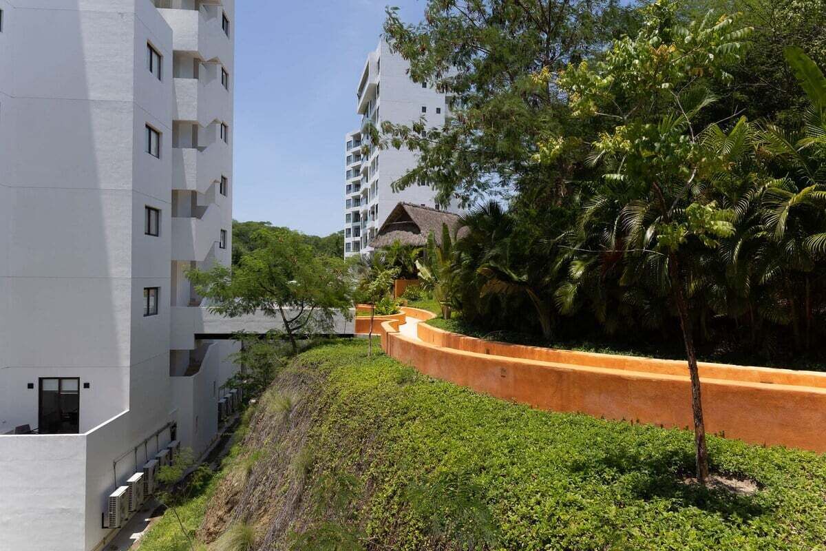 Un edificio moderno de varios pisos, rodeado de abundante vegetación y un sendero curvo.