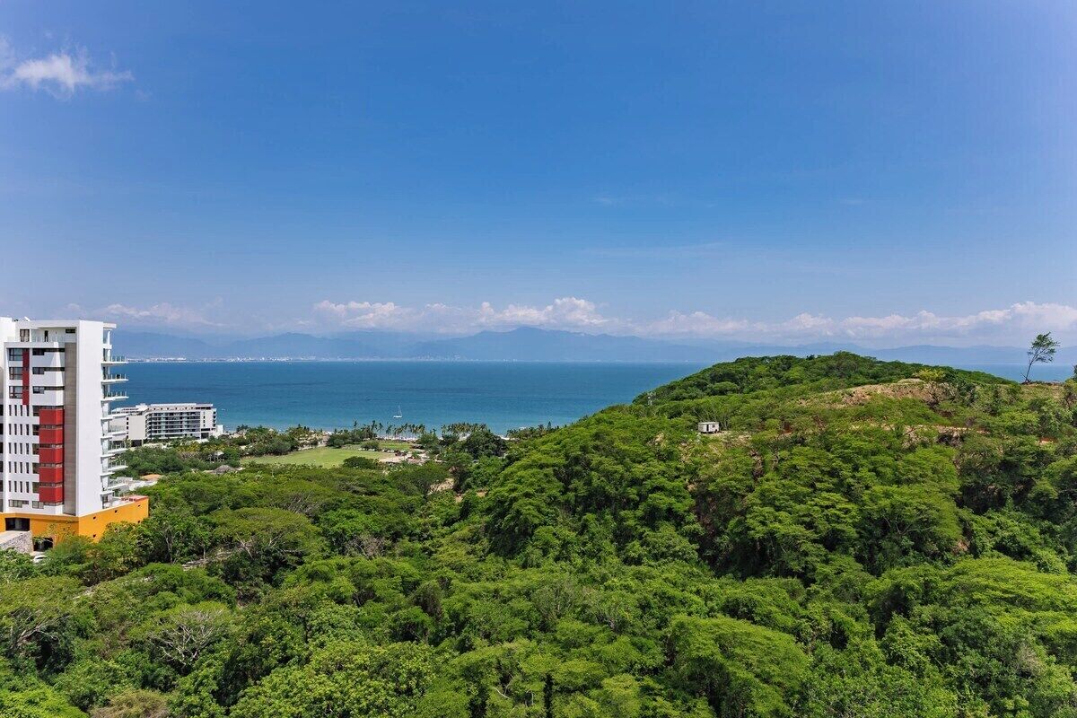 Blick auf die Küste mit einem Gebäude, üppigem Grün und dem Meer im Hintergrund.