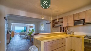 A modern kitchen with wooden cabinets, a microwave, and a stove. There is a dining area with a table and chairs, and a view of the outdoors. - Brand New 2BR Condo With Oceanview - Terrace (Puerto Vallarta)