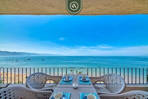 A balcony with wicker furniture, a table set for two, and a view of the sea and beach. - Brand New 2BR Condo With Oceanview - Terrace (Puerto Vallarta)