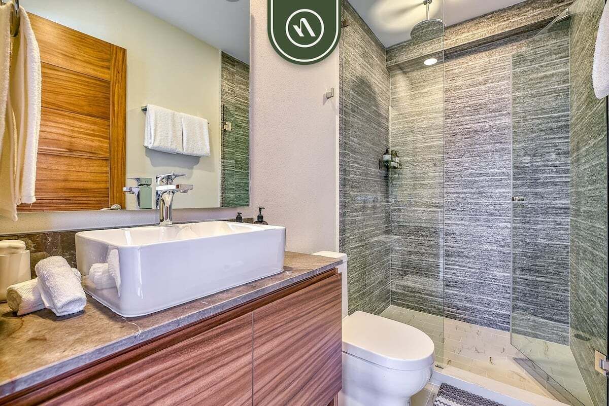 A modern bathroom with a large white sink, wooden vanity, and a glass-enclosed shower area.