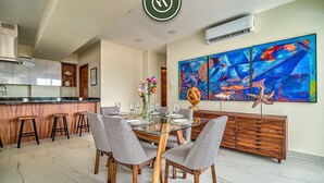A modern kitchen with a dining area, featuring a glass table, grey chairs, and a wooden cabinet.