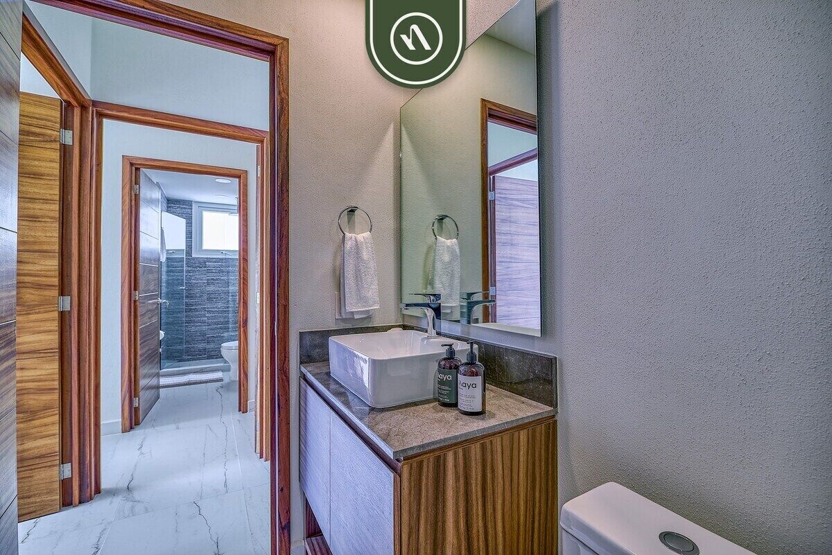 A modern bathroom with a large mirror, a white sink, and wooden cabinetry.