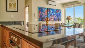 A modern kitchen with a large island, a dining area with a glass table, and a large window with a city view.