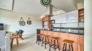 A modern kitchen with a central island, bar stools, and a dining area with a sofa and coffee table.