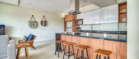 Een moderne keuken met een centraal eiland, barstoelen en een zithoek met een bank en salontafel.