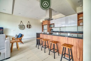 Uma cozinha moderna com uma ilha central, banquetas de bar e um espaço de refeições com sofá e cadeiras.