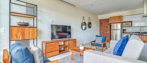 Een moderne woonkamer met een bank, fauteuils, een salontafel, een televisie en een keuken met kasten en apparatuur.