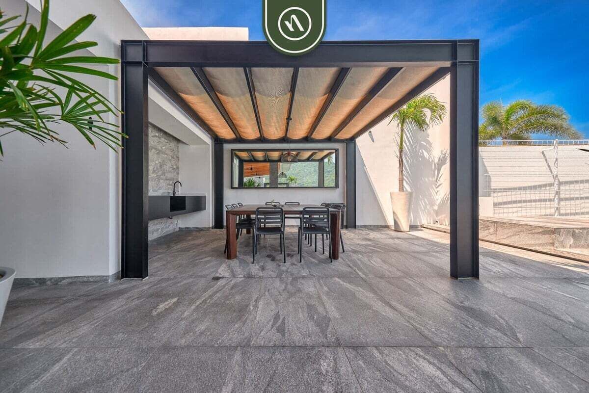 An outdoor dining area with a modern design, featuring a table and chairs under a pergola.