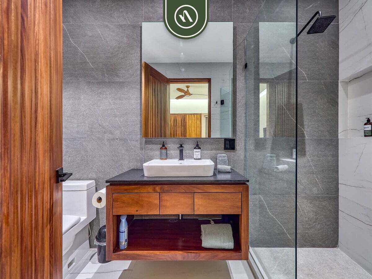 A modern bathroom with a wooden vanity, a large mirror, and a glass shower enclosure.