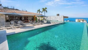 A swimming pool with lounge chairs, a bar area, and a view of the ocean. - Elegant Studio in Romantic Zone - Rooftop Pool (Puerto Vallarta)