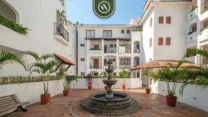 A courtyard with a central fountain, potted plants, and a bench. - Amazing 2 BR Condo Overlooking the Pool - Romantic Zone (Puerto Vallarta)