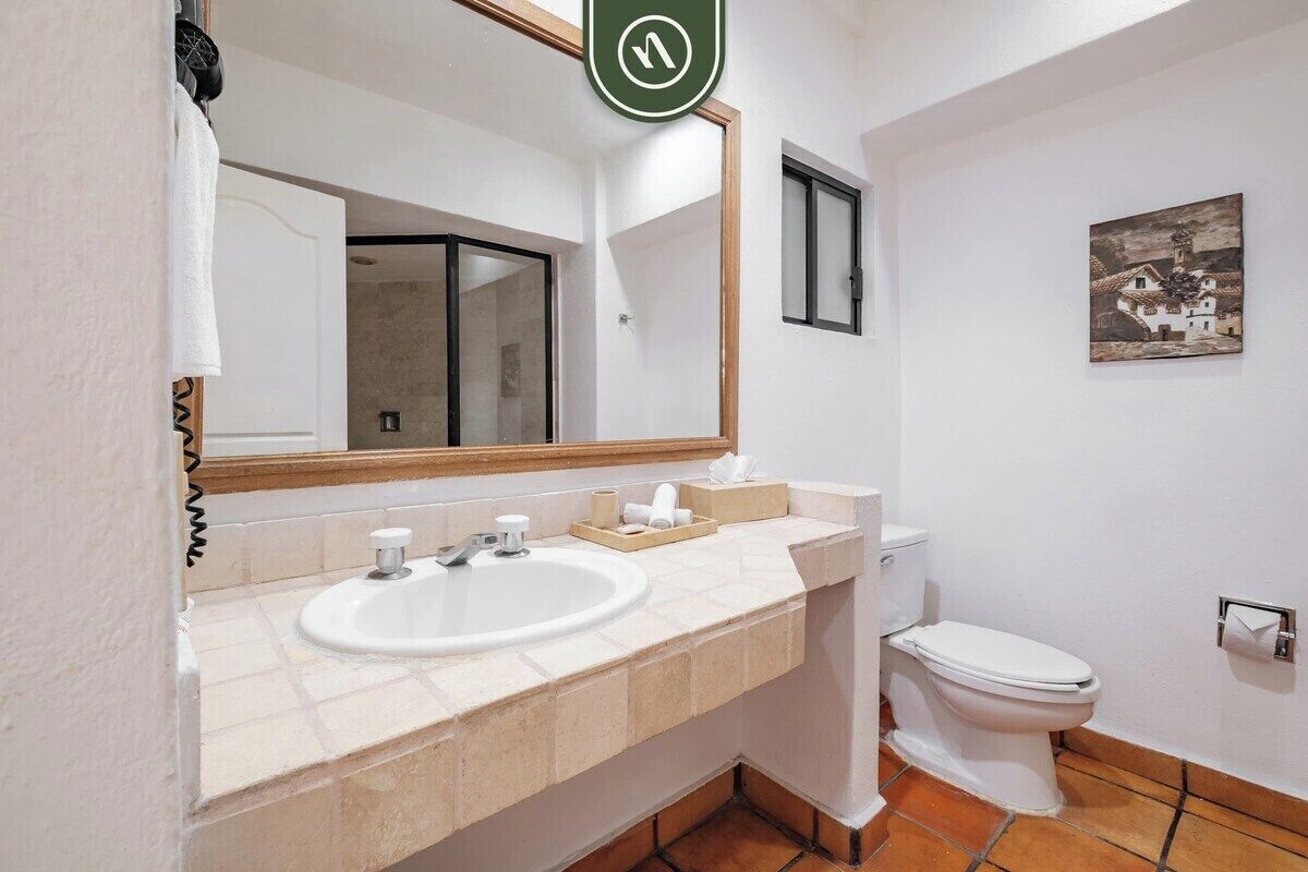 A bathroom with a sink, mirror, toilet, and a small painting on the wall.