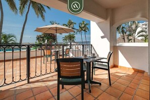 Una terraza con mesa y sillas, vista a la playa y palmeras.