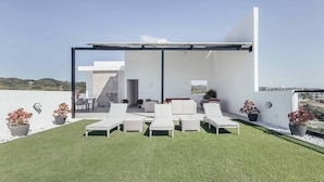 Une terrasse sur le toit, dotée d’un revêtement d’herbe artificielle, de chaises longues blanches et de plantes en pot.