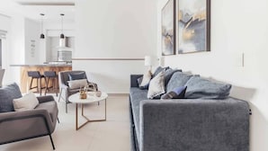 Un salon moderne avec un canapé gris, une table basse et, au fond, un espace cuisine.