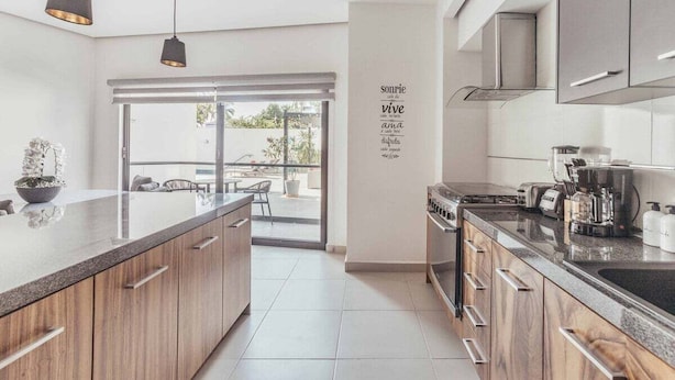 Une cuisine moderne avec des meubles en bois, un grand îlot central et une vue sur l’extérieur.