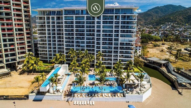 Un hotel con diversi piani, una zona piscina con palme e vista sul paesaggio circostante.