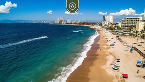 Una playa con vista despejada al océano, una orilla arenosa y el horizonte de una ciudad al fondo.